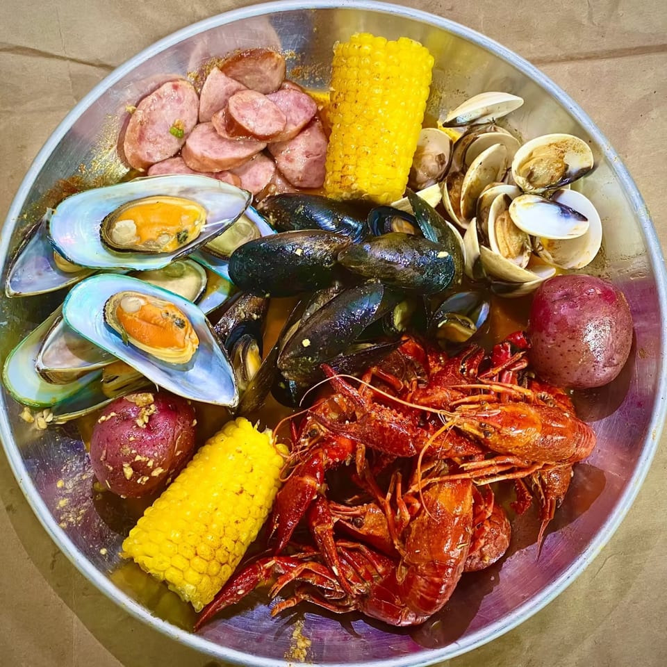 A large seafood boil with mussels, clams, crawfish, sausage, corn on the cob, and potatoes.