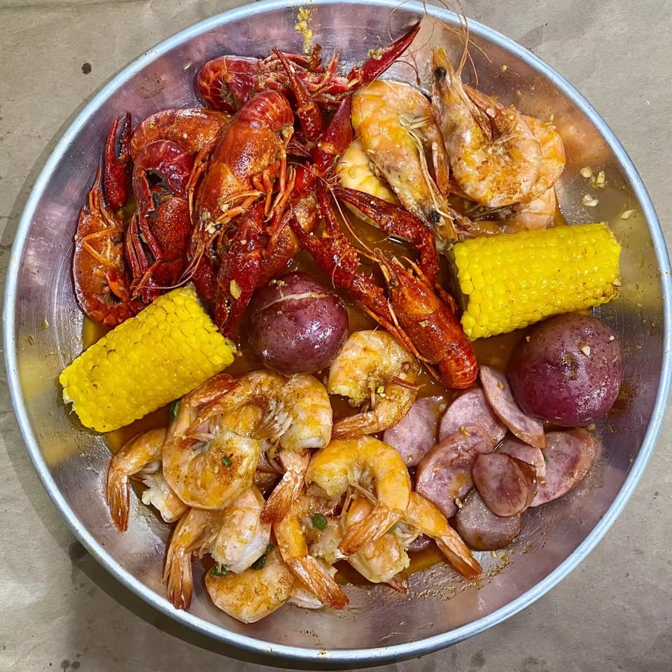 A large metal platter of Cyndy's Seafood boil with crawfish, shrimp, corn, potatoes, and sausage.
