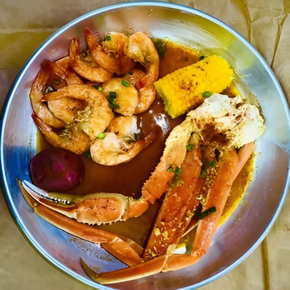 A metal bowl of Cyndy's Seafood with shrimp, crab legs, corn on the cob, and a potato.