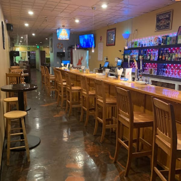 Interior of Cyndy's Seafood bar area with wooden stools, a long bar, and colorful lights.