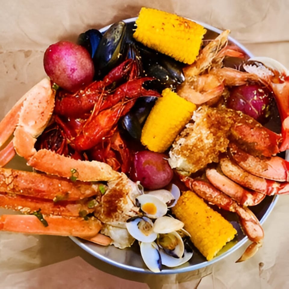 A large platter of Cyndy's Seafood boil with crab legs, crawfish, shrimp, mussels, clams, corn, and potatoes.