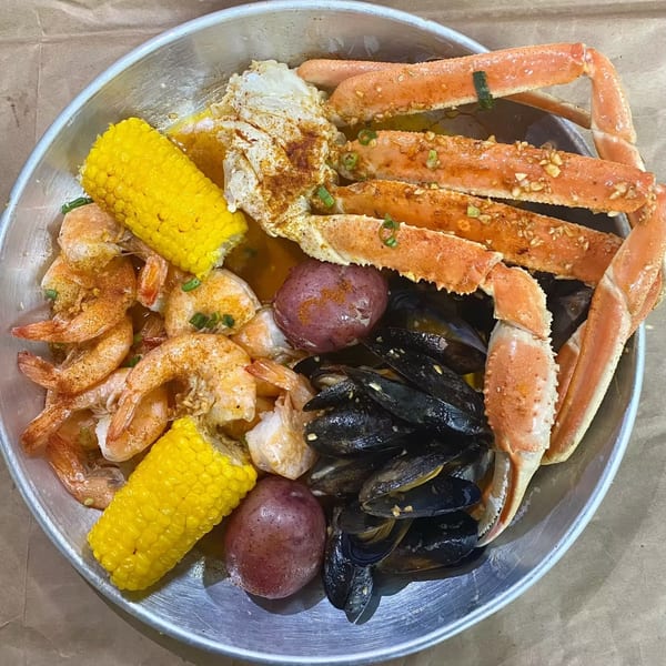 A seafood boil with crab legs, shrimp, mussels, corn on the cob, and red potatoes in a metal bowl.