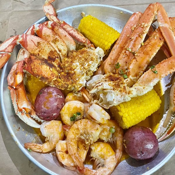 A metal platter of Cyndy's Seafood boil with crab legs, shrimp, corn on the cob, and red potatoes.