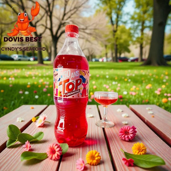 A bottle of red grenadine soda and a glass on a wooden table with flowers in a park.