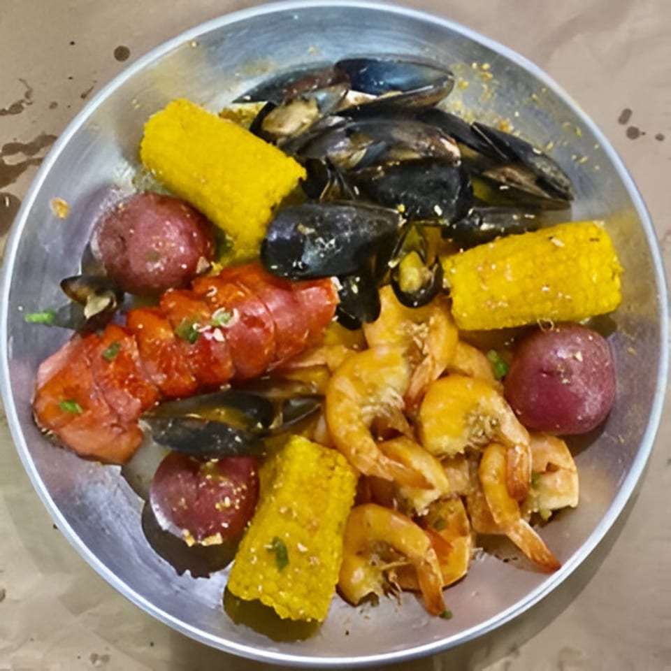 A seafood boil with mussels, shrimp, lobster, corn on the cob, and red potatoes in a metal bowl.