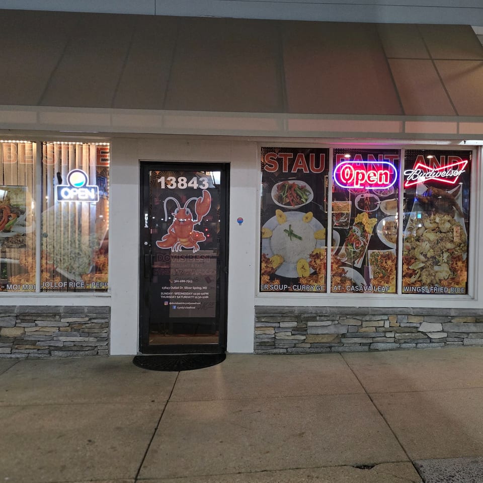 Exterior of Cyndy's Seafood restaurant with neon 'Open' signs and food posters in the windows.