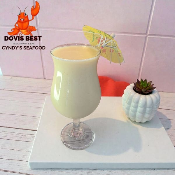 A creamy yellow cocktail with a small yellow umbrella, next to a succulent plant.