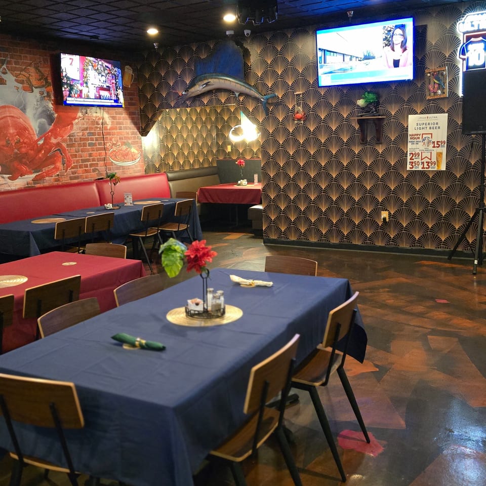 Interior of Cyndy's Seafood restaurant with blue and red tablecloths, a lobster mural, and a mounted fish.