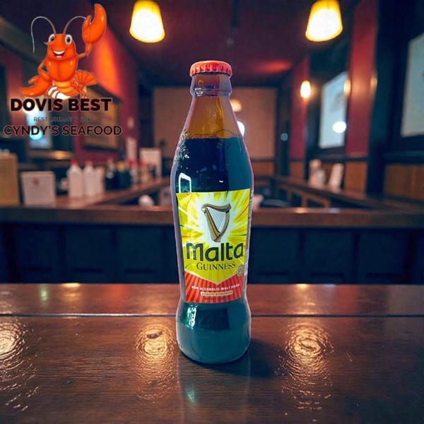 A Malta Guinness bottle on a wooden bar, with the Dovis Best Cyndy's Seafood logo.