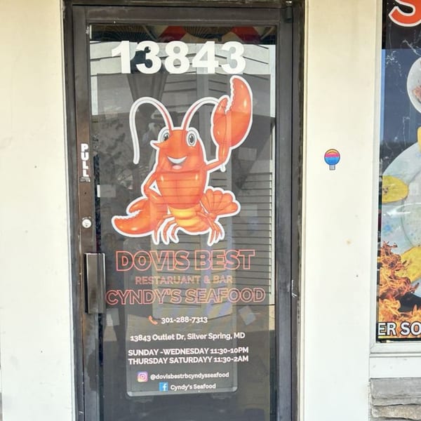 Glass door of Cyndy's Seafood with a cartoon lobster, address, and operating hours.