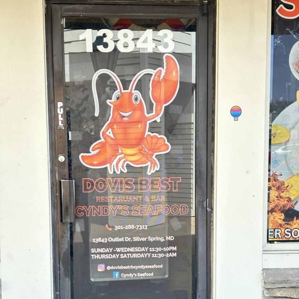 Glass door of Cyndy's Seafood with a cartoon lobster, address, and operating hours.